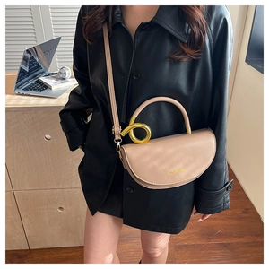 Detail of beige saddle bag featuring a twisted gold metal ring handle and matte leather finish