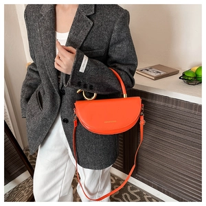 Detail view of bright orange semi-circular saddle bag with golden metal ring handle