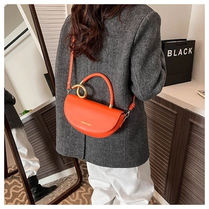 Detail showing orange saddle bag with gold metal ring handle and textured PU leather finish