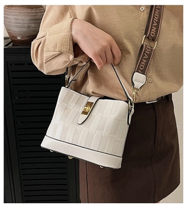 Detail of white bucket bag with wide logo strap and textured surface on a model
