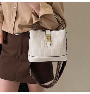 Detail of off-white bucket bag with rectangle texture, gold lock and brown wide strap
