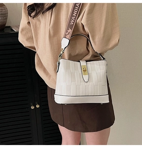 Detail of white textured bucket bag with golden twist lock and patterned wide strap