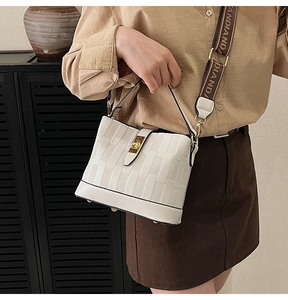 Detail of white bucket bag featuring woven relief texture and wide branded strap