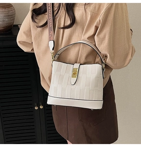 Detail of off-white bucket bag featuring gold twist lock and woven branding strap
