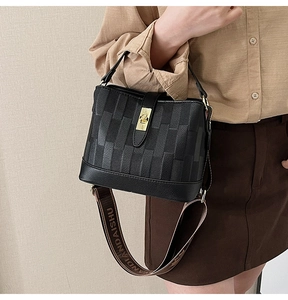 Detail of black leather bucket bag with gold clasp and woven logo shoulder strap