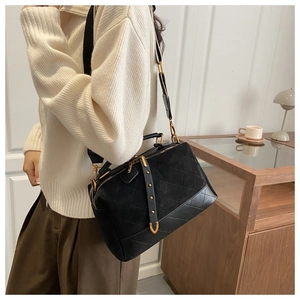 Detail of suede cross-body pillow bag with quilted patterns and gold hardware on a model
