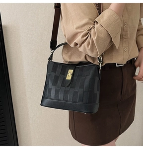 Detail of black embossed bucket bag with gold twist lock and wide fabric shoulder strap