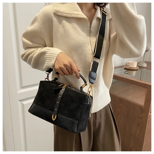 Detail of black suede crossbody bag featuring quilted patterns and gold rivet buckles