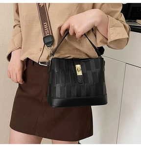 Detail of black bucket bag with woven texture, golden clasp and ISHU logo strap