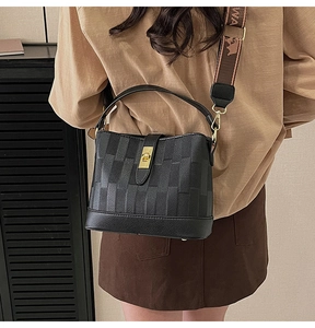 Close-up of black bucket bag with woven texture, golden twist lock and jacquard strap