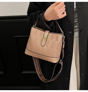 Detail of beige bucket bag with textured pattern, metal twist lock and lettered strap