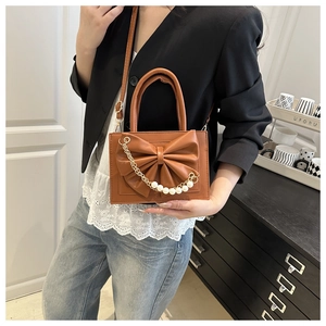 Détail d'un sac à main marron avec nœud en cuir et chaîne perlée sur un modèle