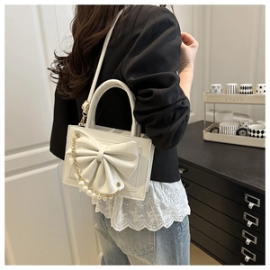 Sac à main en cuir blanc avec nœud en perles et chaîne porté par un mannequin