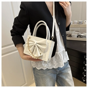 Sac à main blanc en cuir avec nœud et chaîne de perles dans un cadre de vie