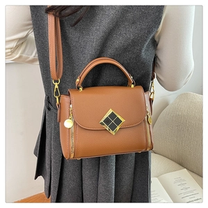 Sac marron à motif litchi avec boucle dorée porté à l'épaule par un mannequin en tenue