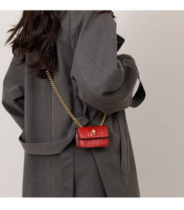 Détail du micro sac rouge à motif croco avec boucle dorée porté sur un manteau long