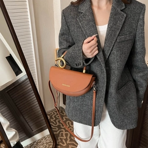 Brown half-moon saddle bag with gold metal handle worn by model in casual suit