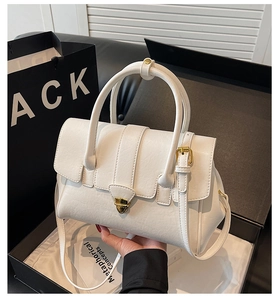 Detail view of white leather handbag with gold trapezoid lock and accordion side gussets