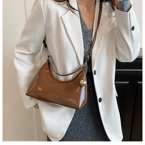 Détail d'un sac hobo en cuir verni marron avec breloque boule dorée et logo fashion