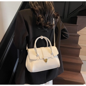 Detail of elegant white leather handbag with gold lock clasp and slim crossbody strap