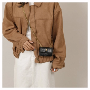 Détail d'un mini sac noir à texture crocodile avec boucle tête de mort dorée et chaîne