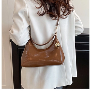 Detail van glanzende donkerbruine lakleren hobo tas met een gouden bolvormige hanger