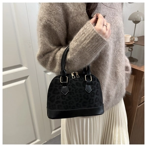 Close-up of leopard print shell bag with golden hardware held by a model in a cozy room