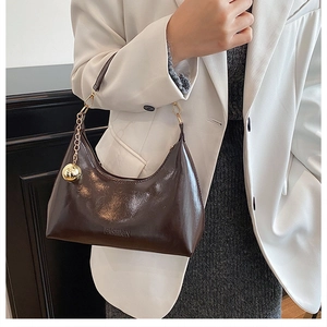 Détail du sac hobo en cuir verni marron foncé avec breloque boule dorée et chaîne