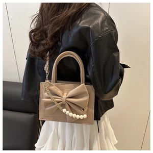 Détail du sac à main beige élégant avec nœud décoratif, chaîne perlée et poignées