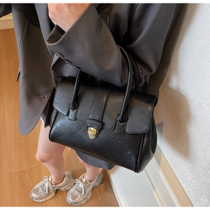 Detail of black pebbled leather handbag with gold shield buckle and top handle