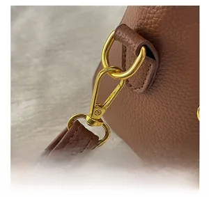 Gros plan sur la boucle dorée et la lanière en cuir grainé marron du sac à main
