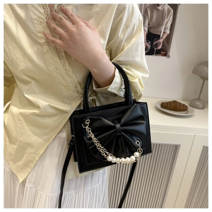 Détail du sac à main noir avec nœud papillon, chaîne perlée et cuir synthétique