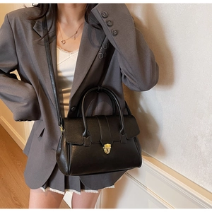 Detail shot of black tote bag with gold lock and handles worn with a grey blazer