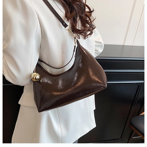 Détail du sac à bandoulière en cuir verni marron brillant avec breloque sphérique dorée