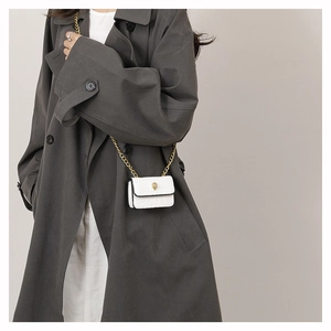 Mini sac blanc à motif crocodile avec tête de lion dorée porté sur un manteau gris