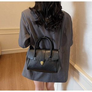 Detail of minimalist black leather briefcase with vintage gold buckle on a grey blazer