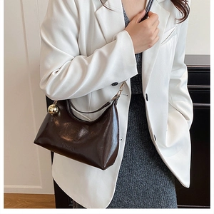 Détail d'un sac hobo en cuir verni marron foncé avec pendentif boule dorée et relief