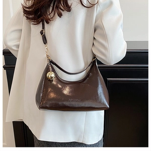 Détail d'un sac hobo en cuir verni marron chocolat avec un pendentif sphérique doré