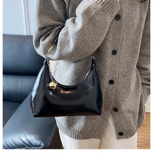 Détail d'un sac demi-lune en cuir verni noir avec charme sphère dorée et logo gravé