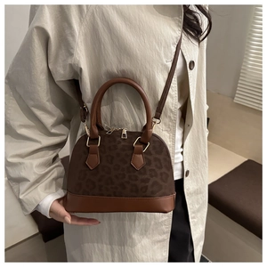 Lifestyle shot of a leopard print shell bag worn as a shoulder purse with brown leather trim