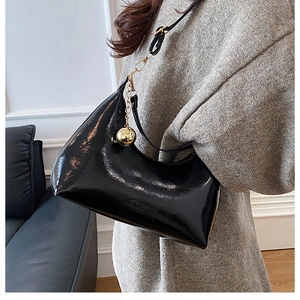 Détail du sac en cuir verni noir avec breloque boule dorée et logo de mode gravé