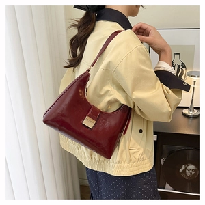 Close-up of glossy wine red underarm bag with gold metallic square buckle on model