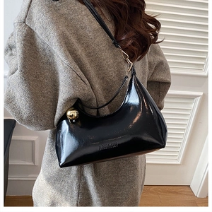 Detail of black patent leather crescent bag with gold sphere charm and fashion embossed logo