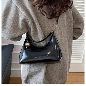 Détail du sac à bandoulière noir brillant avec gaufrage et pendentif boule dorée