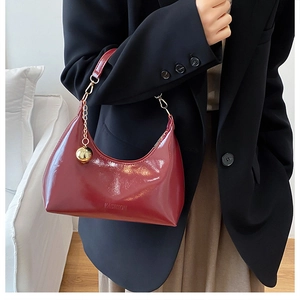Détail du sac croissant en cuir verni bordeaux avec breloque boule dorée et chaîne