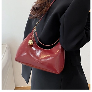 Detail of burgundy patent leather hobo bag with gold ball charm and fashion logo