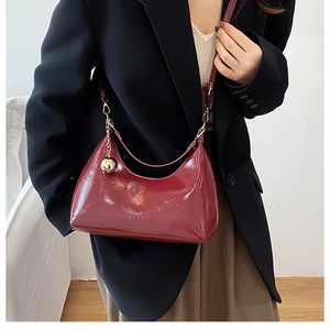 Gros plan d'un sac hobo en cuir verni rouge avec breloque boule dorée et logo gravé