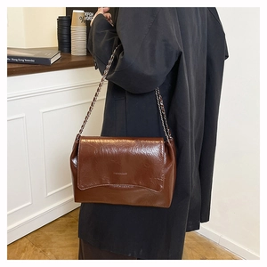 Detail of vintage brown textured leather shoulder bag with gold chain and embossed logo