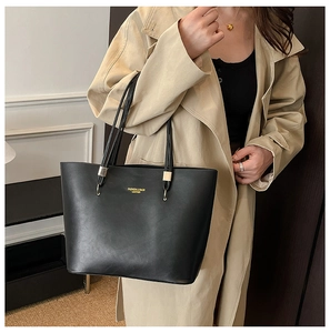 Detail of black PU leather tote bag featuring gold hardware and logo on shoulder strap