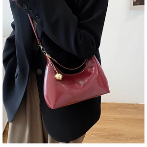 Close-up of glossy deep red crescent bag with gold chain and spherical pendant detail